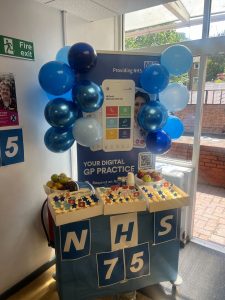 A stand celebrating the NHS' 75th birthday with cake and balloons in white and blue. 